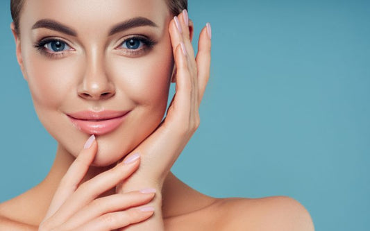 Visage d'un jeune femme avec très belle peau et ongles. elle à une mains sur le côté de son visage et l'autre sur son menton et son poignet. le fond est bleu