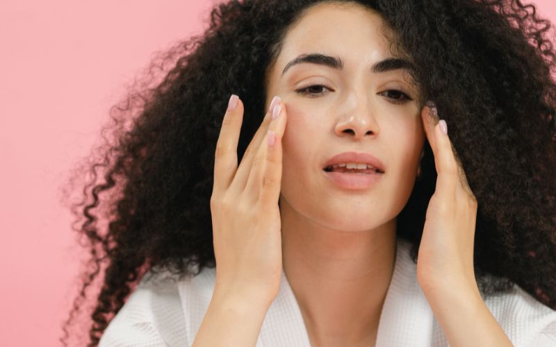 Jeune femme brune avec les mains prêt du visage, avec ses annulaires sur ses pommettes.